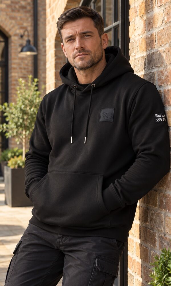 Male model wearing the AJ Stealth Hoodie in a sunlit courtyard, front view