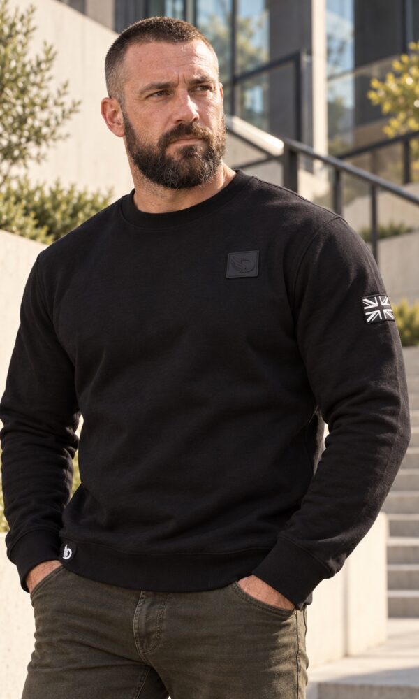 Man wearing the AJ Stealth Sweatshirt outdoors, front view showing chest patch and sleeve flag