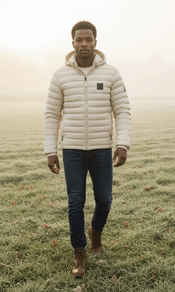 Full-body walking shot of a man wearing the DROW Wear cream padded coat, stepping forward across a frosty field.