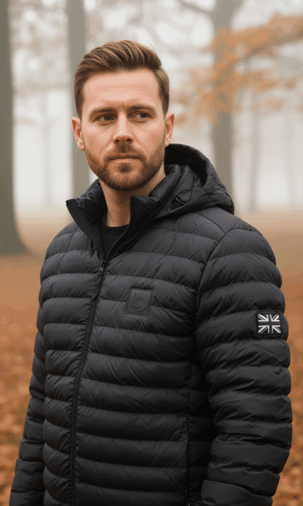 Man wearing a black padded DROW Wear coat with British military-inspired Union Jack patch, standing in an autumn forest.