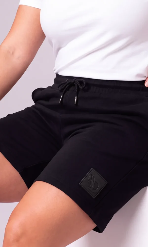 Seated woman wearing DROW Black Premium Shorts with a drawcord waist, side pocket and tonal DROW leg patch